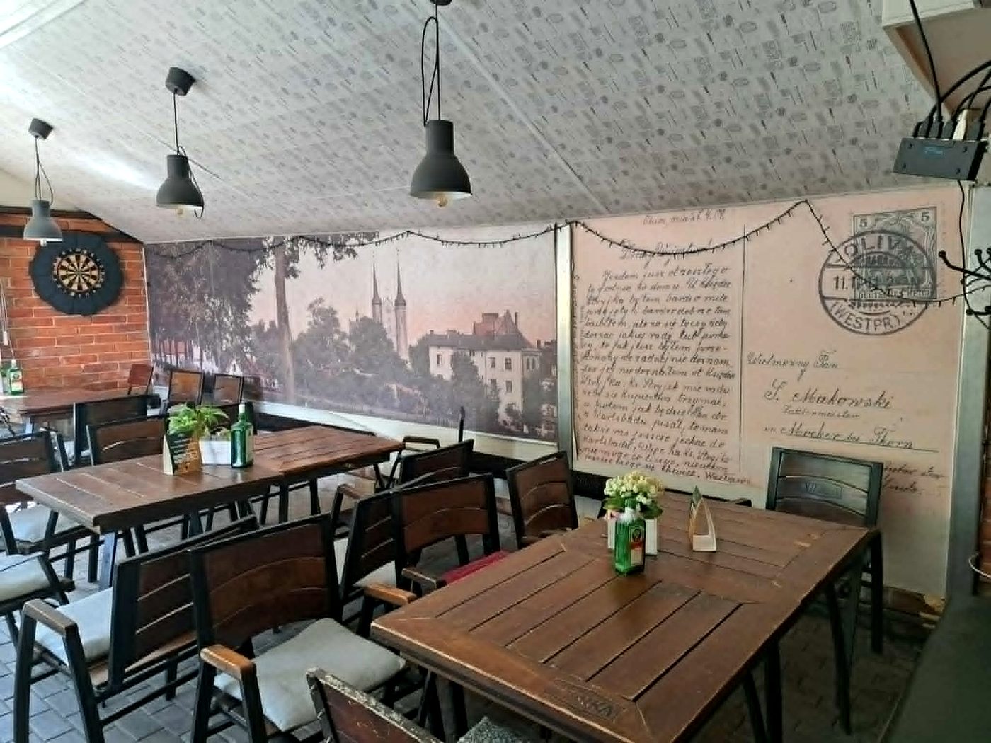 Przytulne wnętrze Grill Bar Merc z drewnianymi stołami i historyczną grafiką Oliwy na ścianie